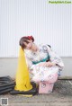 A woman in a kimono sitting on the ground next to a traffic cone.