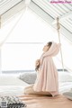 A woman sitting on a bed wearing a pink hooded robe.