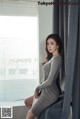 A woman in a gray dress sitting on a window sill.