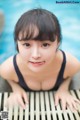 A woman in a black bathing suit leaning on a wooden bench.