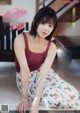 A woman in a red tank top and floral skirt sitting on a ledge.