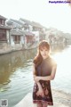 A woman in a black dress standing by a body of water.