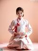 A woman in a white and red hanbok sitting on a bed.