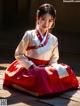 A woman in a red and white hanbok sitting on a wooden floor.