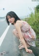 A woman in a white dress crouching down on the side of a road.