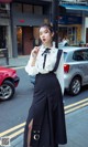 A woman in a white blouse and black skirt is standing on the street.