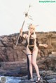 A woman dressed as a demon holding a spear on a rocky beach.