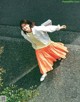 A woman in an orange skirt and a white jacket is posing for a picture.