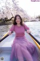 A woman in a pink sweater and purple skirt sitting in a boat.