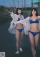 Two young women in blue bikinis walking down a road.